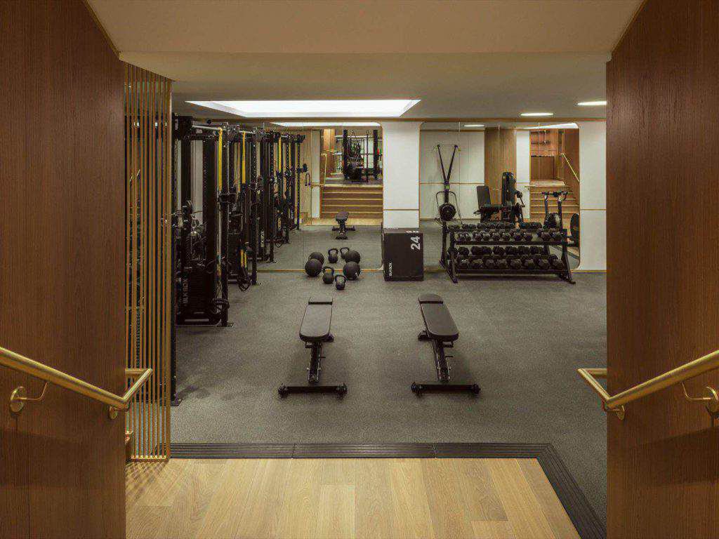 Ein moderner Fitnessraum mit Bänken, freien Gewichten, Medizinbällen, Kettlebells, Fitnessgeräten und Holzakzenten an Wänden und Böden.