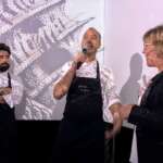 Zwei Köche und Moderatorin bedanken sich nach dem Event bei den Gästen. Im Hintergrund wird ein lebendiges TastEmotion-Bild projiziert, das die Sinne des Publikums anspricht und eine spannende Szenerie schafft.