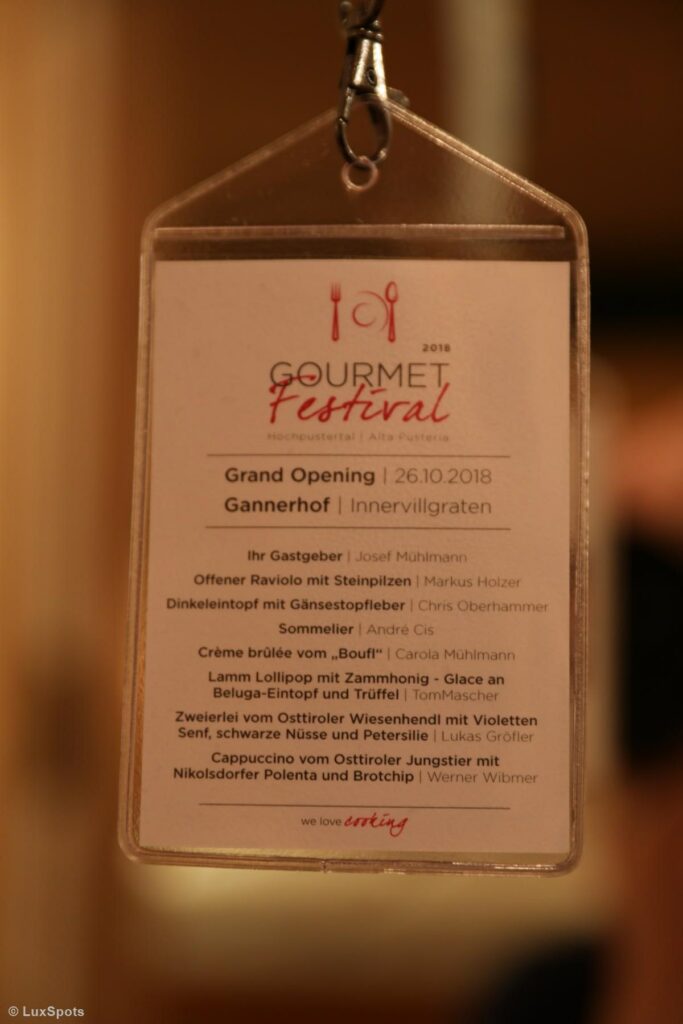 Ein Event-Badge für das Gourmetfestival 2018 mit Auflistung der Köche und Gerichte, darunter Ravioli, Gnocchi und Lamm, mit der großen Eröffnung am 26.10.2018 im Gannerhof, Innervillgraten.