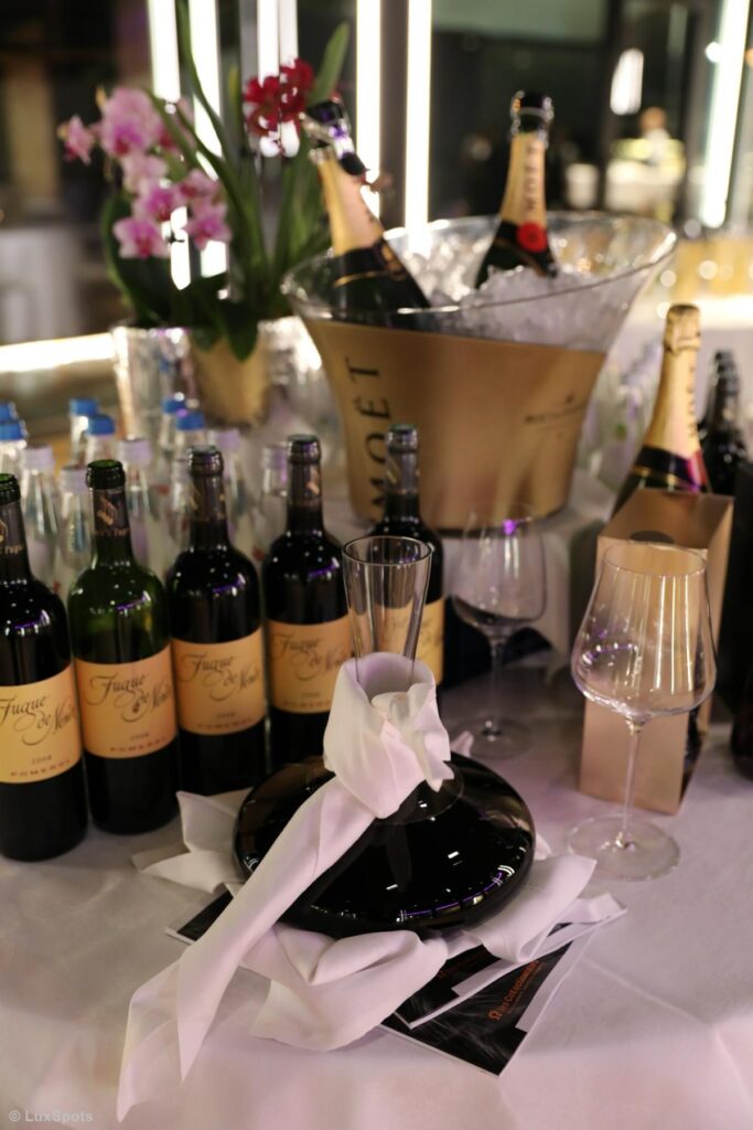 Ein Tisch mit mehreren Flaschen Wein und Champagner, einer Karaffe mit weißer Schleife, Gläsern und Orchideen im Hintergrund.