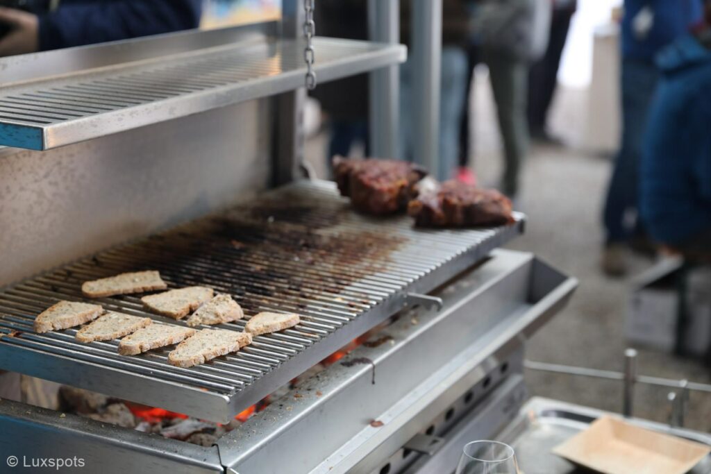Grill mit Brotscheiben und Fleisch, umgeben von Menschen.