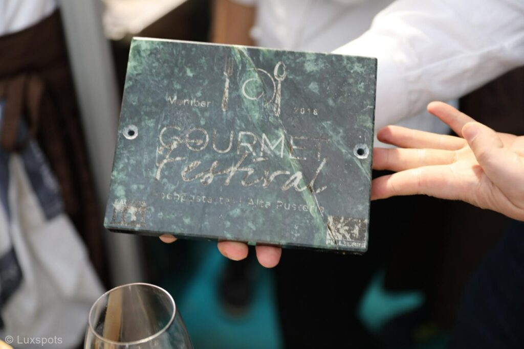Eine Hand hält eine Ehrentafel mit der Gravur „Gourmet Festival 2018“.