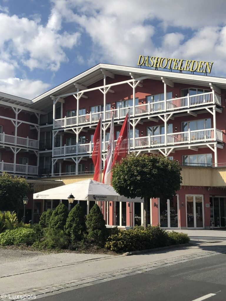 Außenansicht des Hotel Eden in Seefeld, Tirol. Davor ist ein Parkpltz sowie ein rundgeschnittener Baum und ein großer Sonnenschirm zu sehen.