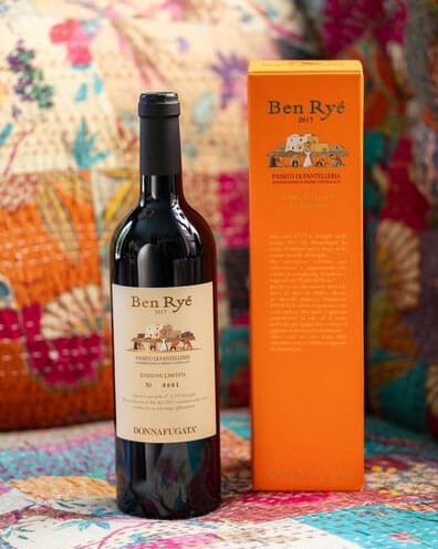 Eine Flasche Ben Ryé 2017-Wein steht neben ihrem orangefarbenen Karton auf einer bunt gemusterten Oberfläche.