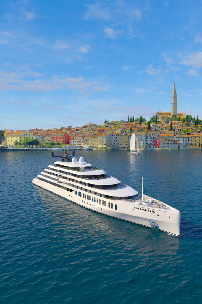 Eine Luxusyacht segelt in der Nähe einer Küstenstadt mit farbenfrohen Gebäuden und einem hohen Turm.