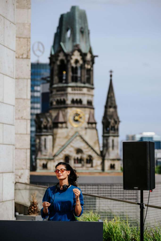 Eine Person mit Kopfhörern steht auf einem Dach mit der Kaiser-Wilhelm-Gedächtniskirche im Hintergrund.