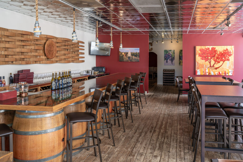 Bar auf Holzfässern mit Tischen und Hockern sowie mit Gemälden und dekorierten Wänden, einem hängenden Fernseher und Deckenleuchten.