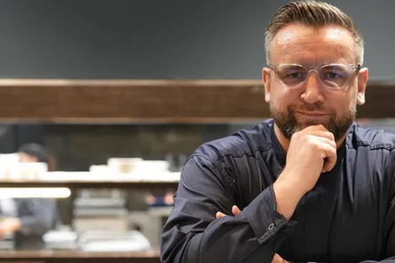 Ein Mann mit kurzen Haaren, Brille und Bart stützt sein Kinn auf die Hand, während er in einer modernen LuxSpots-Küche steht.